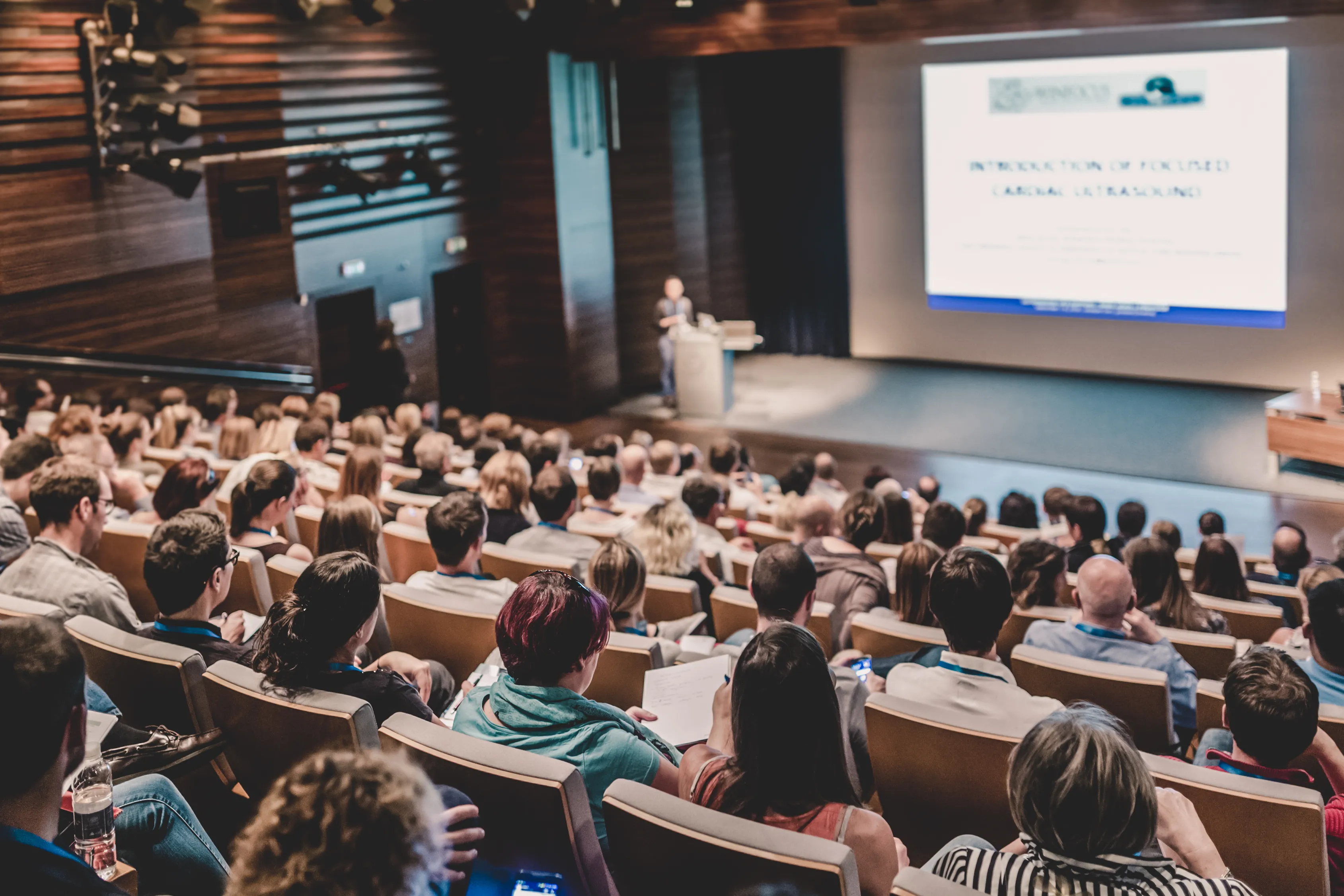 Publiek in een conferentiezaal tijdens een symposium met live muziek.